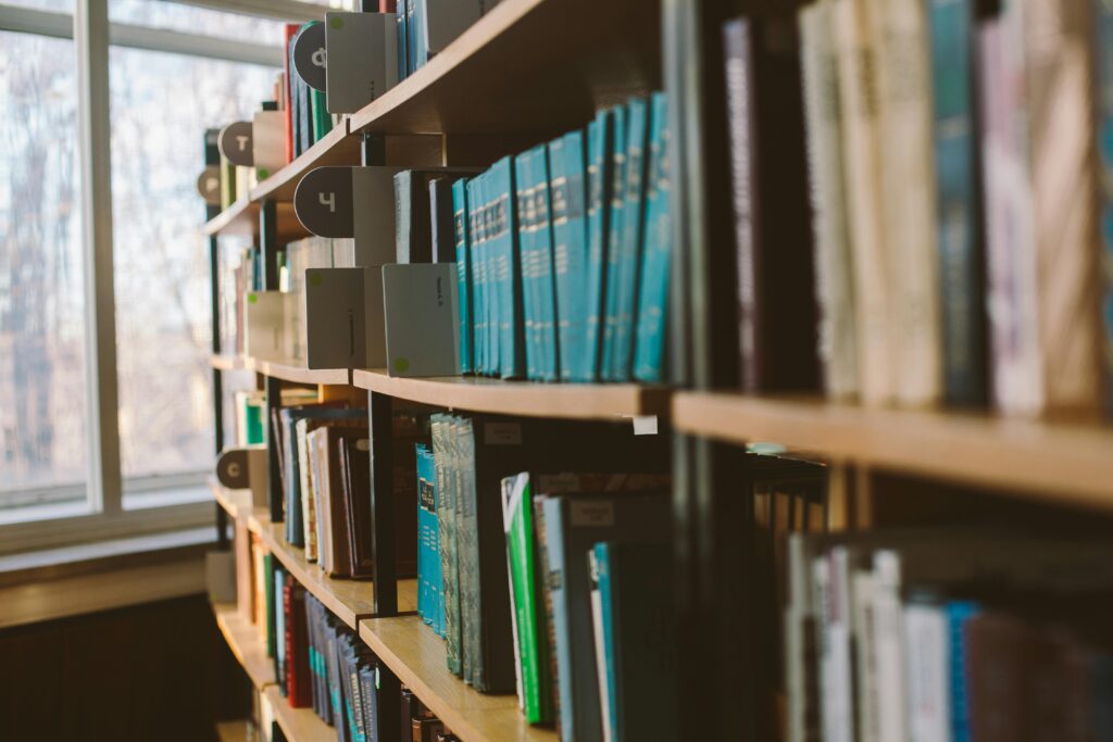 Close-up view of organized books on a library shelf with sunlight streaming through windows.