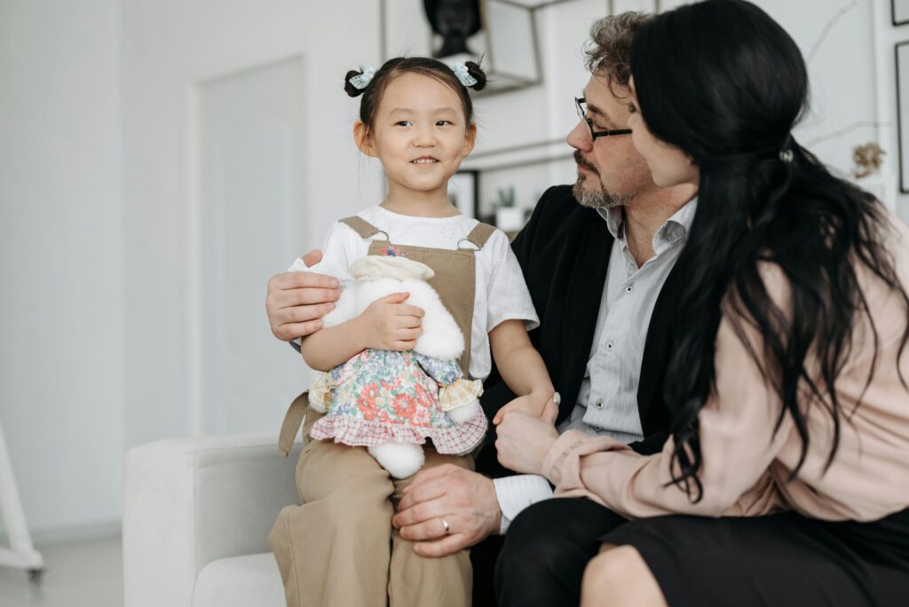A joyful family scene with adopted child cuddling a stuffed toy indoor setting.