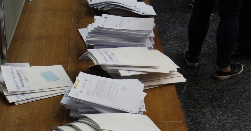 Stacks of documents neatly arranged on a wooden desk indoors, reflecting office organization.