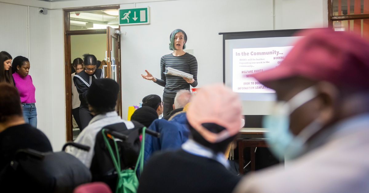 A diverse group attending a community meeting with a presenter speaking in front of a screen.