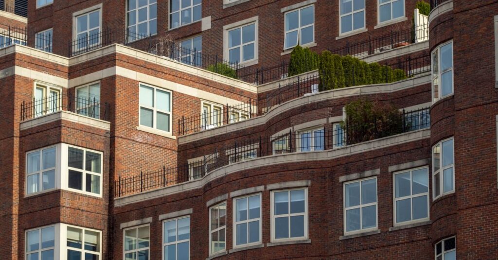 Detailed view of a red brick apartment building with terraces and greenery.