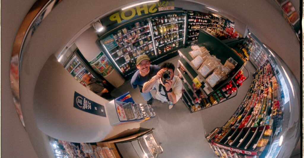 Fisheye mirror reflection capturing a supermarket aisle filled with various products and a visible photographer.