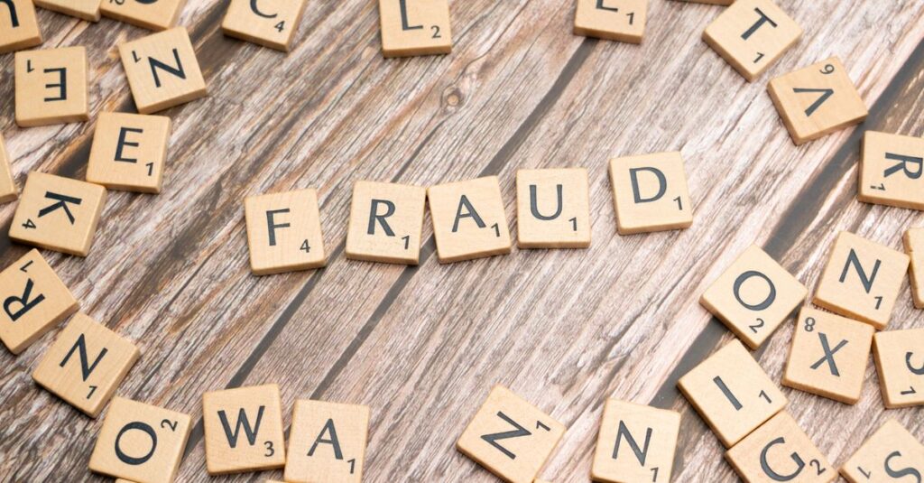 Alphabet tiles arranged to spell 'fraud' on a wooden surface, symbolizing deception.