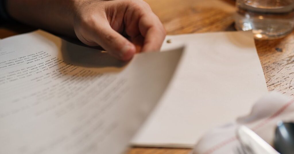 Close-up of a person reading a document at a wooden table with a glass of water.