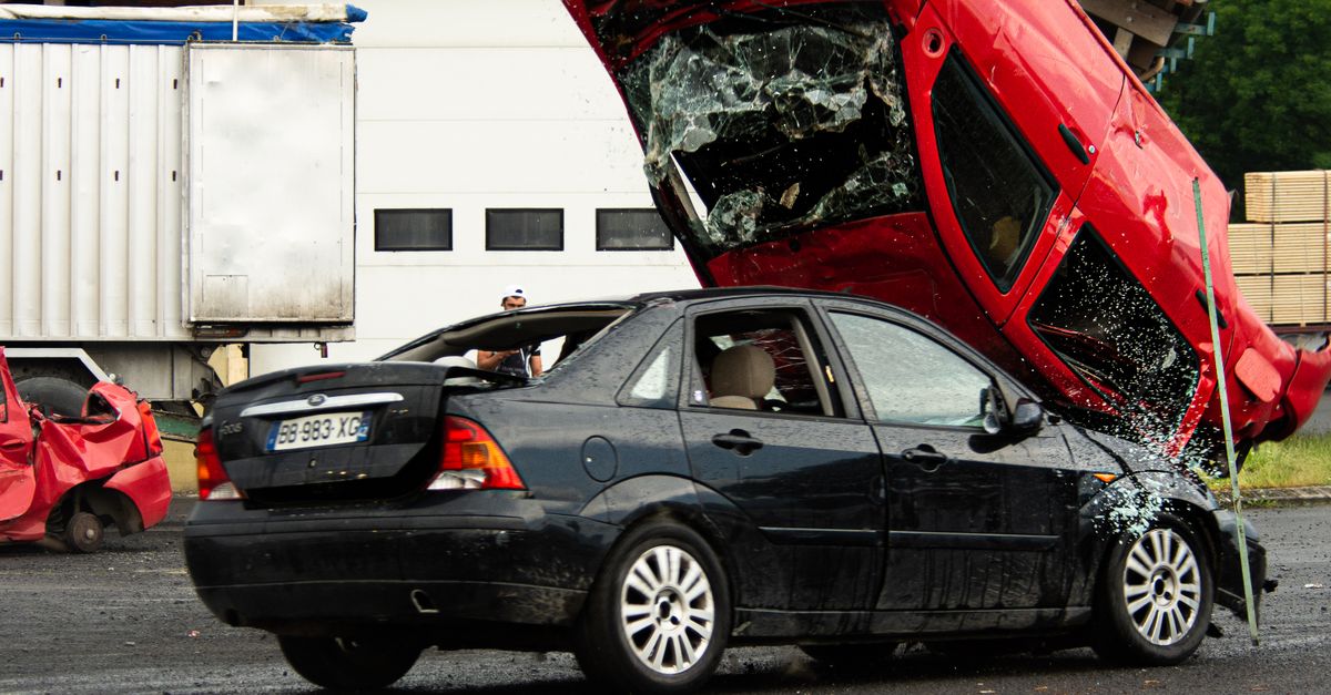 A thrilling car stunt crash with a red car flipped onto a black vehicle in an outdoor setting.