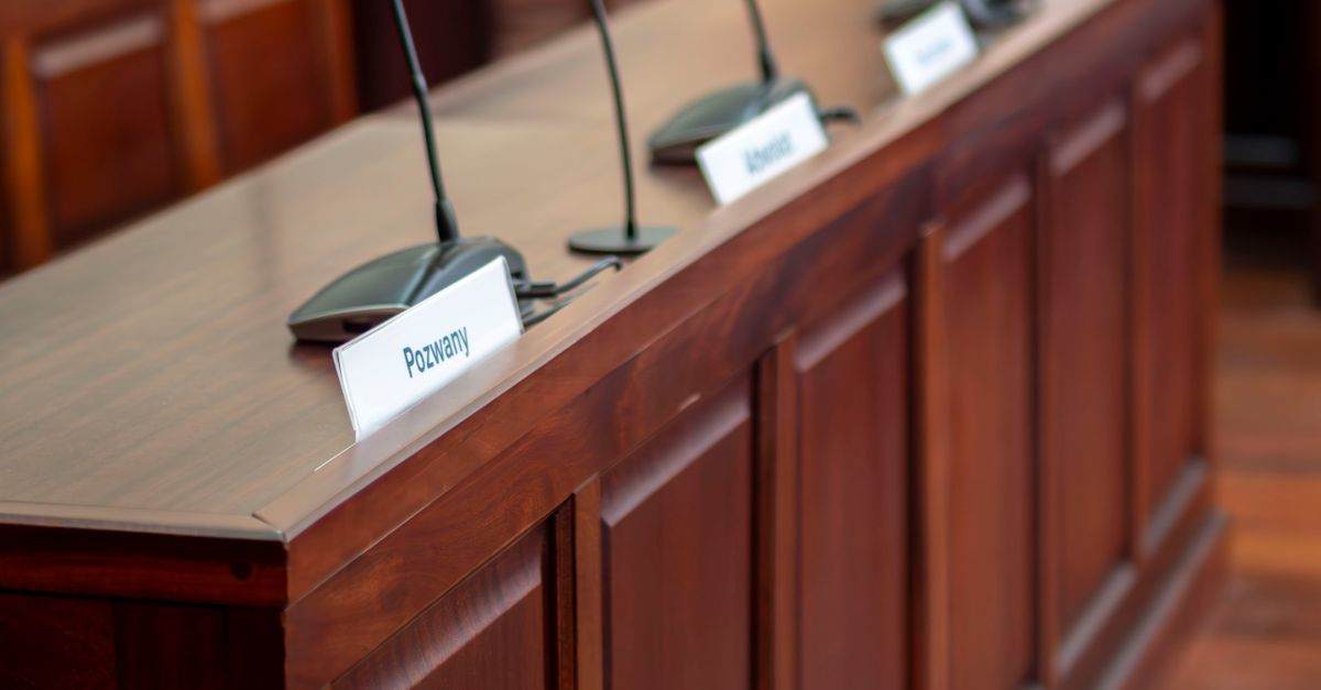 Empty courtroom desk with microphones and nameplates in a Polish court setting.