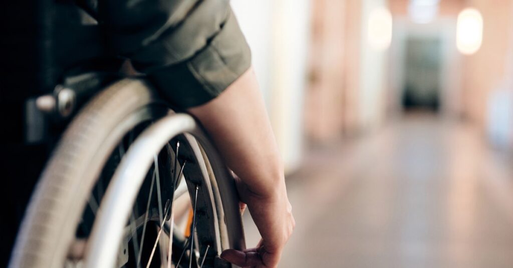A person in a wheelchair is navigating an indoor hallway, focus on the wheel and hand.