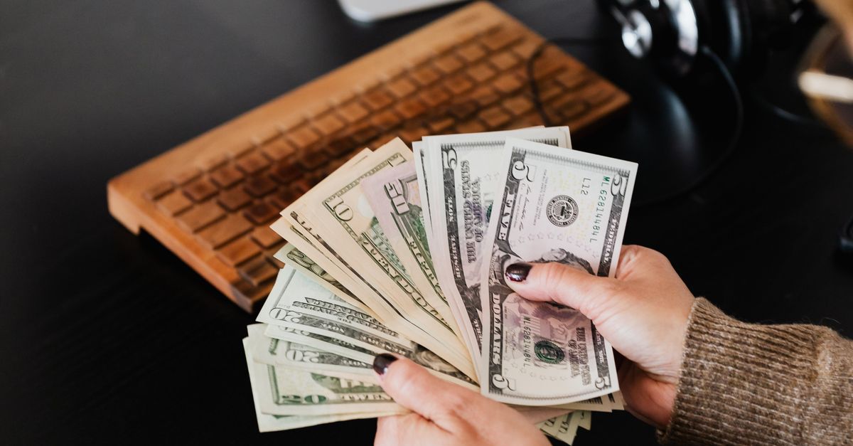 Close-up of hands counting dollar bills at a desk with computer and planner.