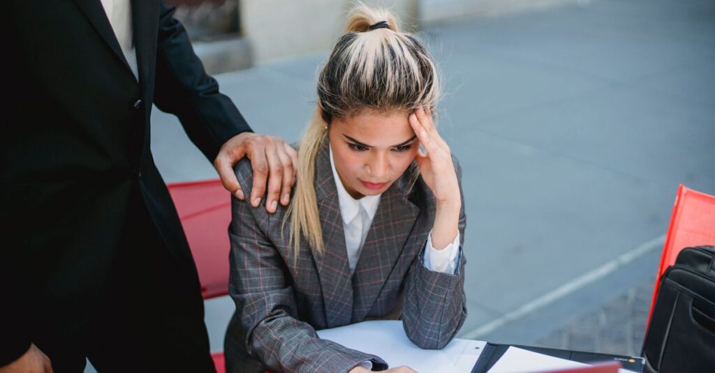 Businesswoman in stress at outdoor table, seeking support from colleague.