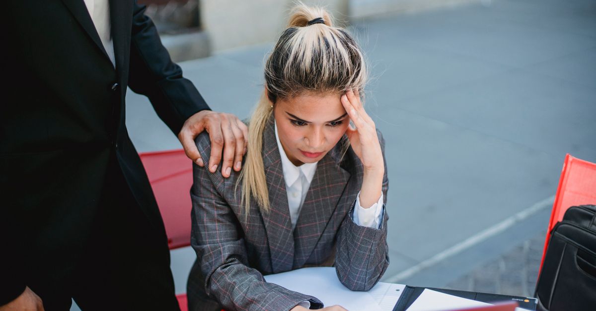 Businesswoman in stress at outdoor table, seeking support from colleague.
