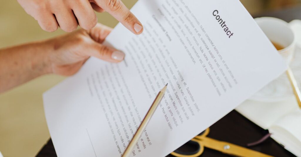Hands pointing at contract on desk with laptop, indicating collaboration