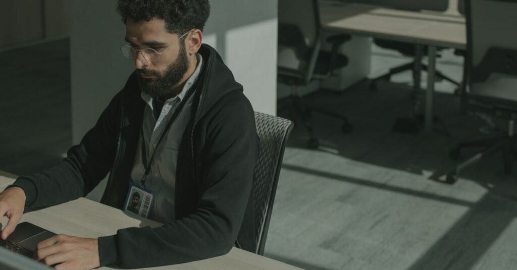 Bearded man working on a computer indoors, focused on cybersecurity tasks.