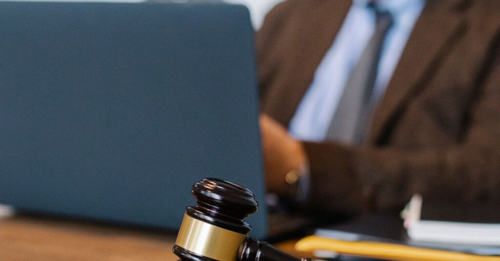 Blurred male lawyer in formal suit sitting at table with modern netbook and decorative gavel