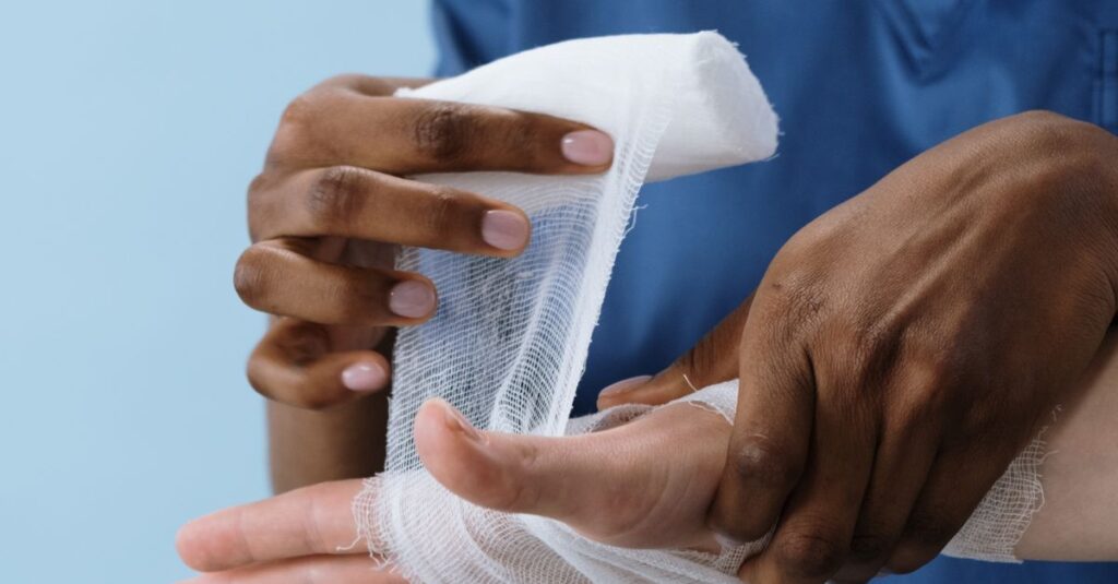 A healthcare professional wrapping a patient's hand with gauze for injury care.