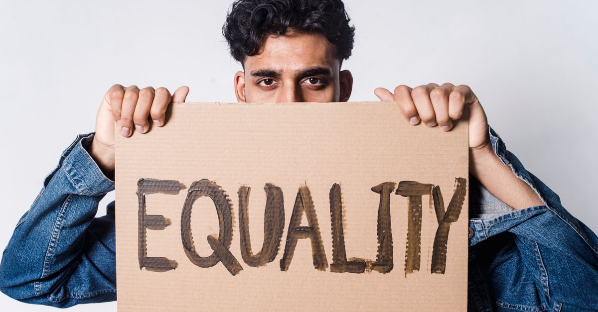 A man holds a cardboard sign reading 'EQUALITY' in a studio.