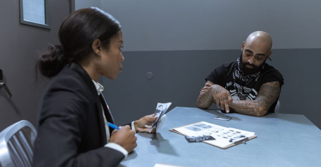 Police officer interrogating a suspect in an investigation room with documents and evidence on the table.