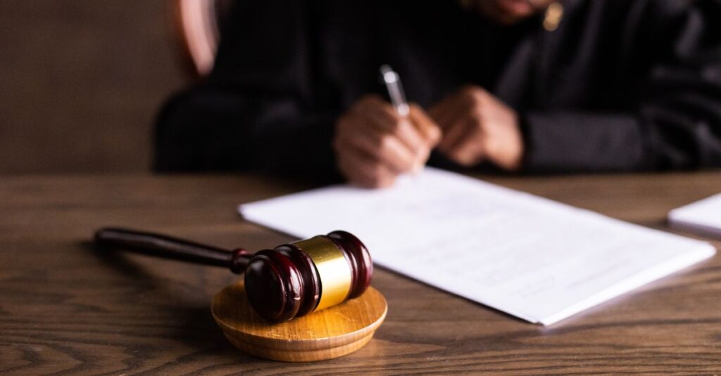 Judge signing documents at desk with focus on gavel, representing law and justice.