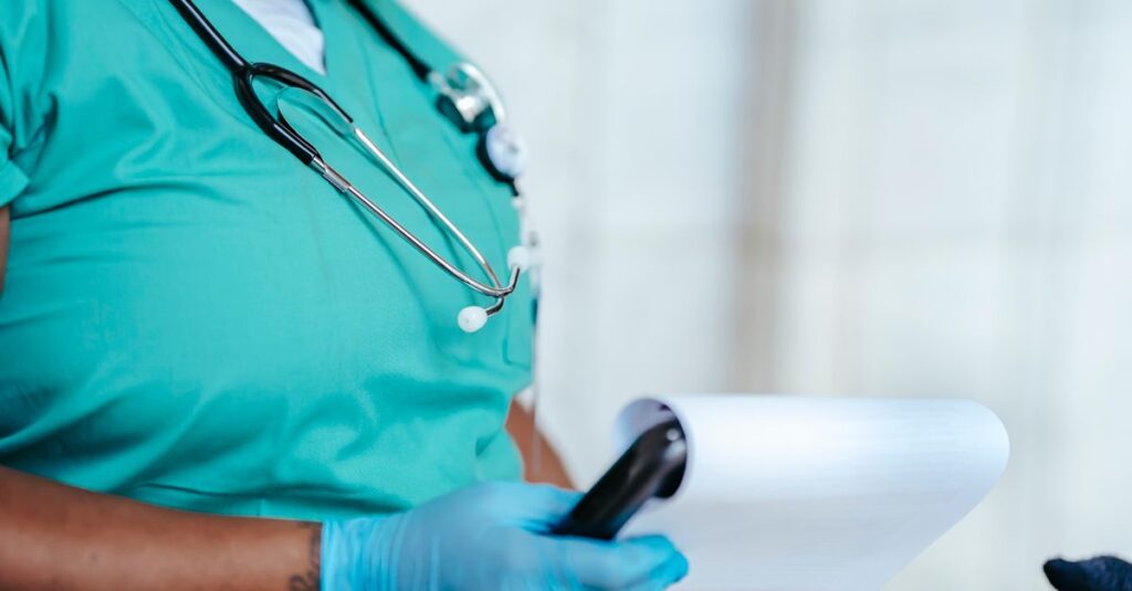 Side view of crop anonymous tattooed ethnic female medic in uniform with stethoscope and papers on clipboard