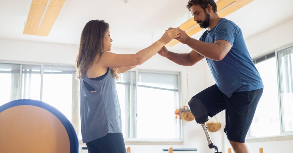 A man with a prosthetic leg exercises with a therapist in a well-lit gym environment.