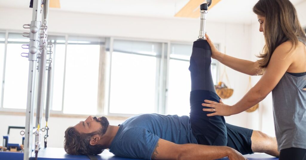 Personal trainer assists amputee in rehabilitation exercise indoors.