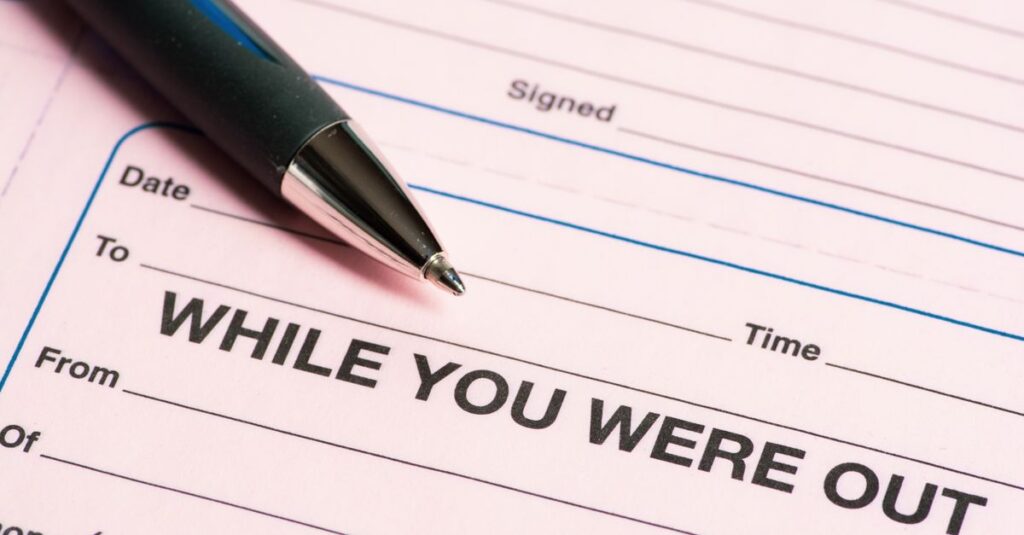 Close-up of a pen and 'While You Were Out' message pad, emphasizing office communication.