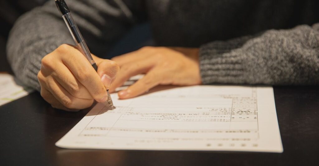 Crop anonymous male in gray sweater writing in form of important document at table