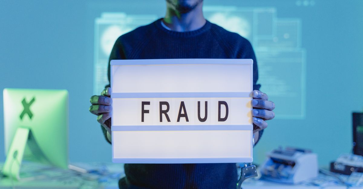 A man holding a sign reading 'FRAUD' in a tech environment, highlighting cybersecurity concerns.