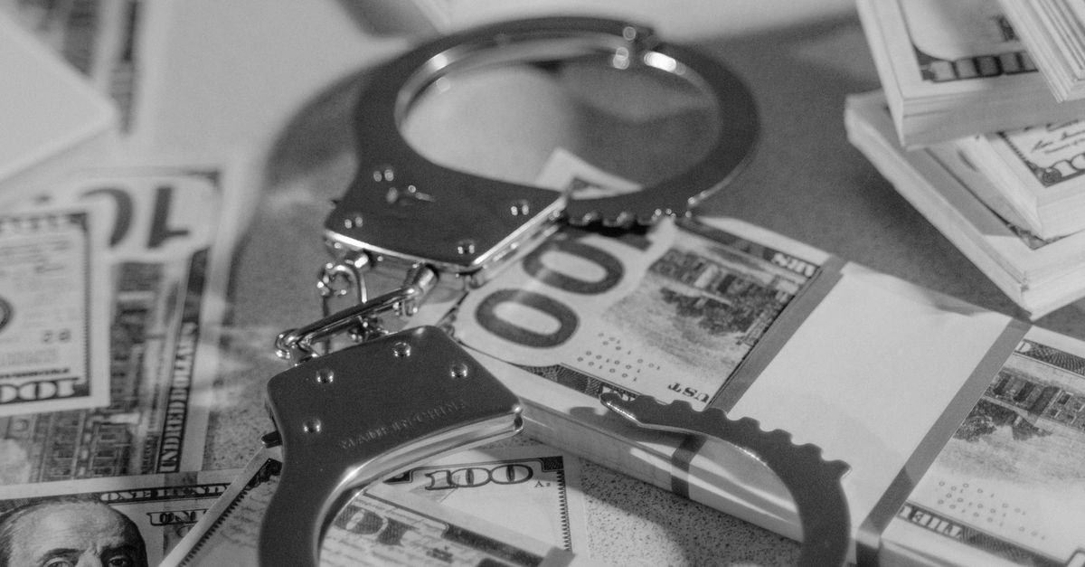 Black and white image of handcuffs placed over stacks of US dollar bills, symbolizing financial crime.