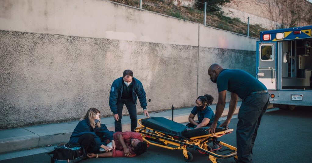 Emergency team helps an injured person on the street with a stretcher nearby.