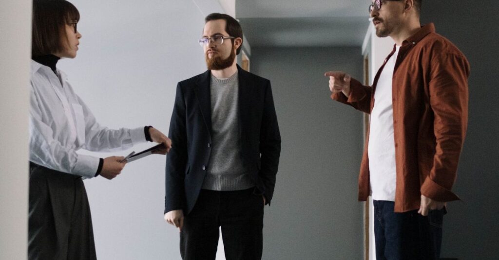 Three professionals engaged in conversation in a modern office corridor.