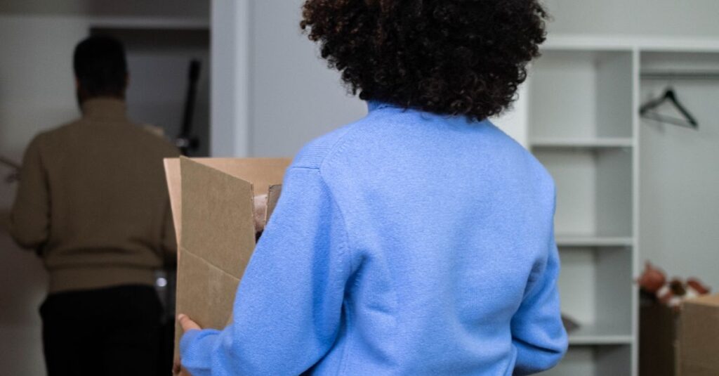 Rear view of woman carrying box in home during move-in day, emphasizing moving and relocation theme.