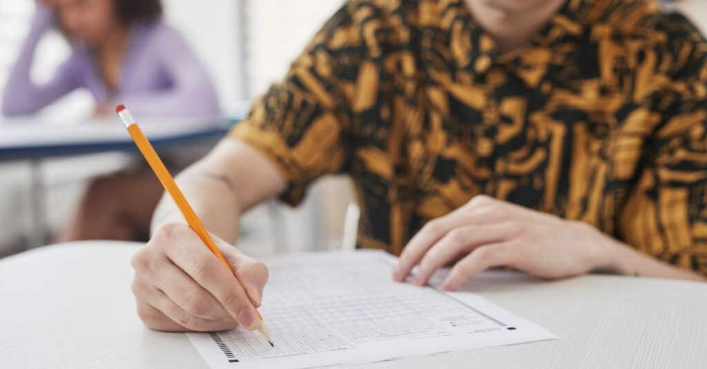 Young adult writing on exam paper in classroom setting, focus on pencil and paper.