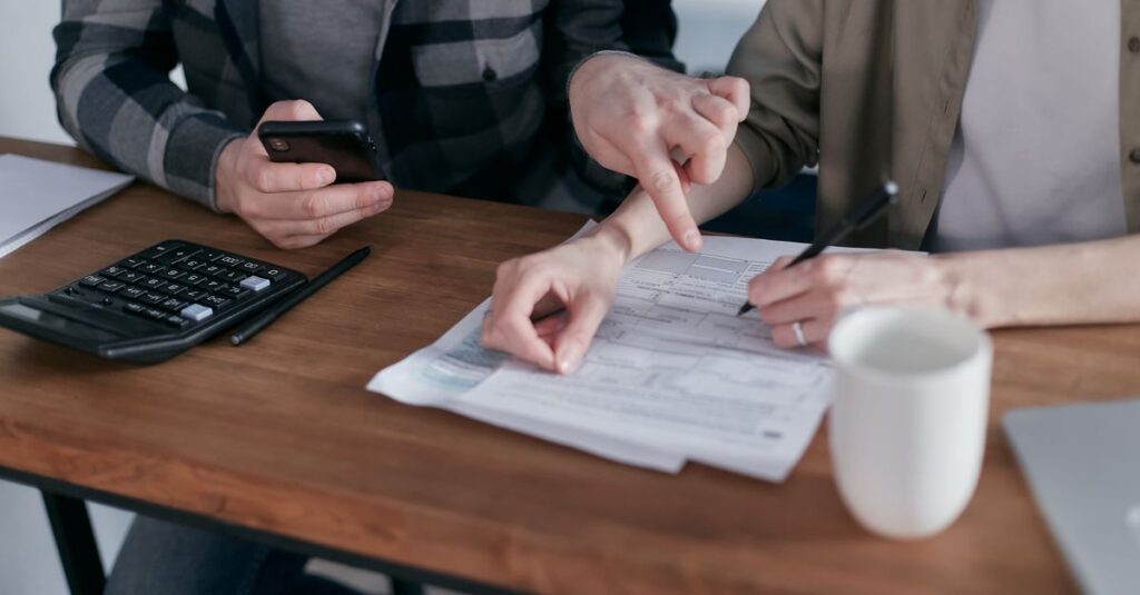 A couple analyzing financial documents and using a calculator at a home table.
