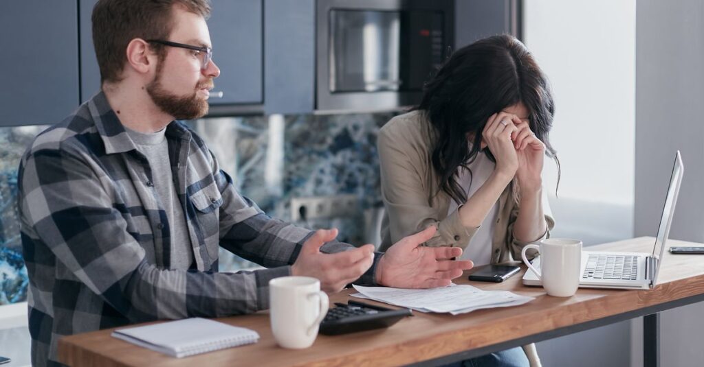 A couple seated at a table, looking stressed while discussing financial issues indoors.