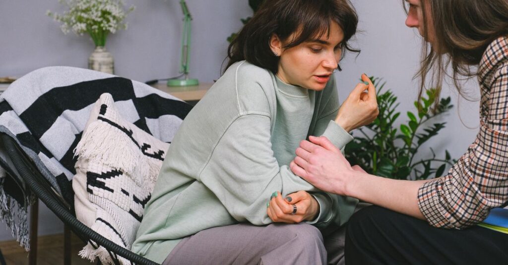 Crop psychotherapist holding adult woman by arm while talking during psychological session in light house