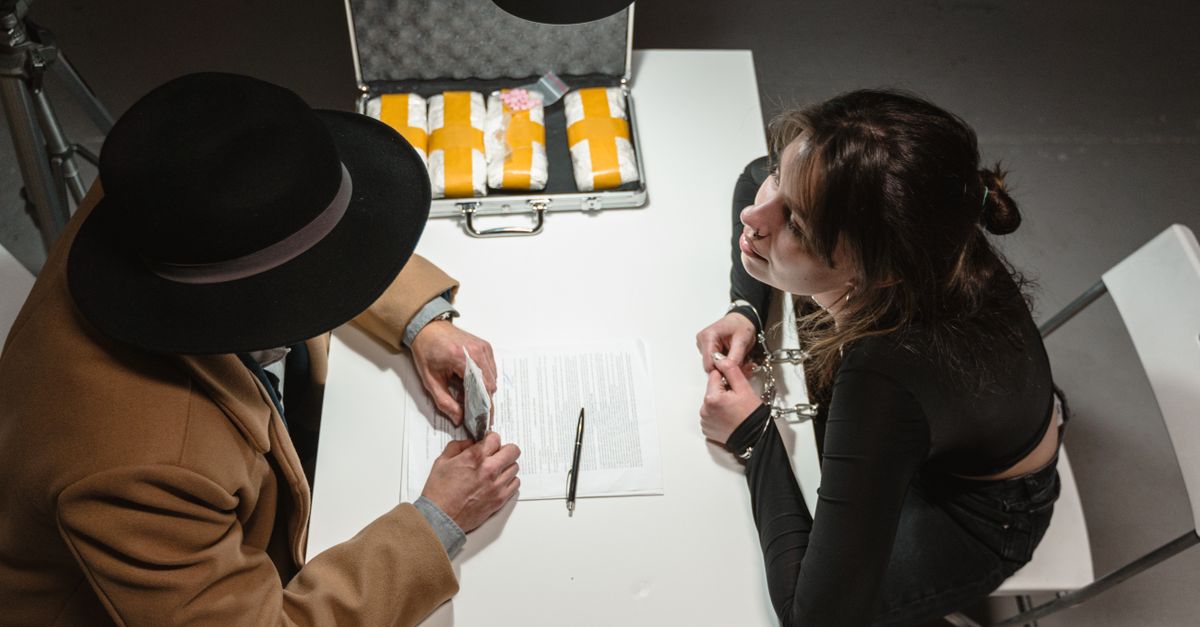Two individuals engage in a tense negotiation with a briefcase of suspicious packages in a dimly lit room.