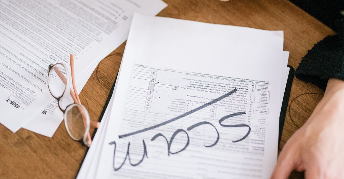 Close-up of hands reviewing suspicious tax documents labeled 'scam' on a desk.