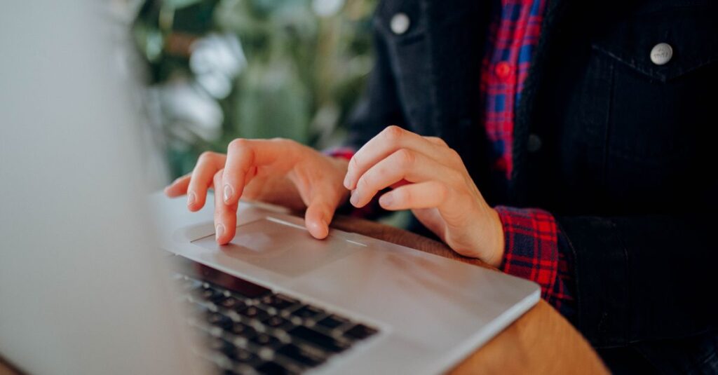 Person wearing a plaid shirt typing on a laptop keyboard indoors, focusing on hands and device.