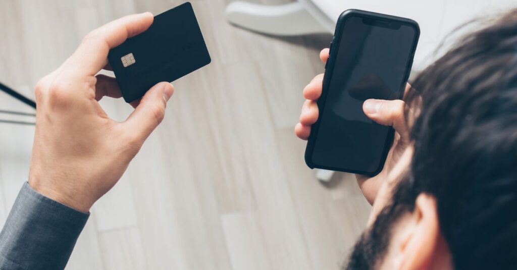 Close-up of man holding a smartphone and credit card, making an online payment indoors.