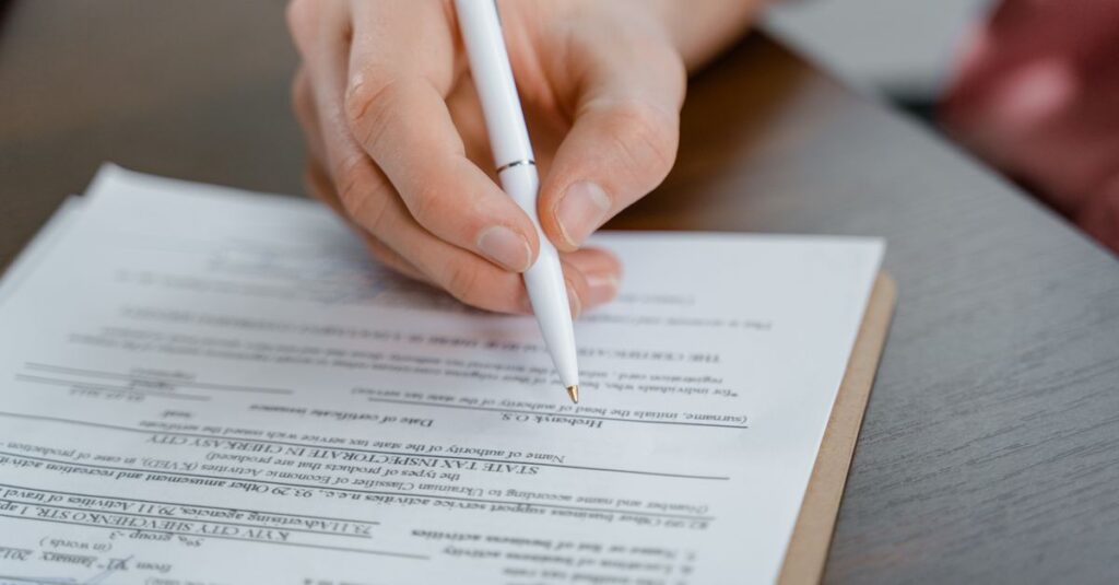 A hand holding a pen signing a document, close-up shot with focus on the paper.