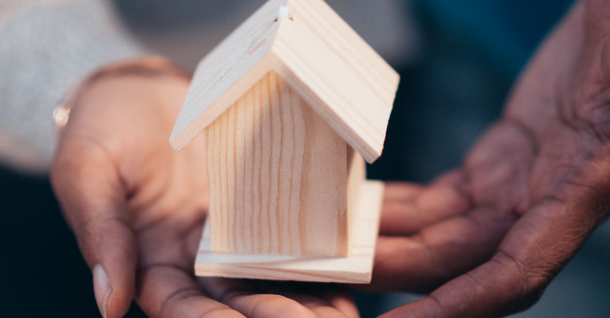 Close-up of hands holding a wooden house model representing real estate or new home purchase.