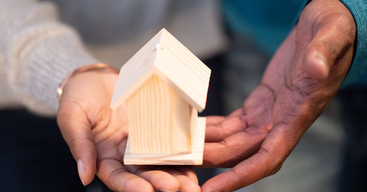 Hands holding a small wooden house model, symbolizing new home ownership and real estate transactions.