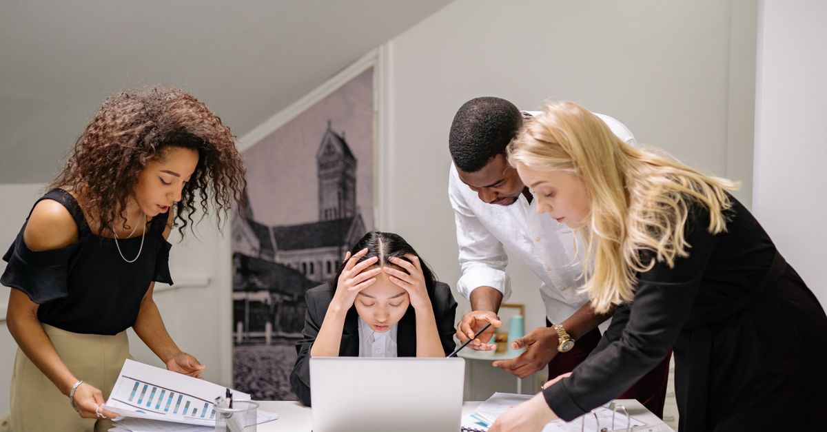 Diverse group of coworkers engaged in a collaborative office meeting, discussing around a laptop.