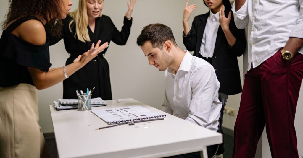 A team confronts a stressed colleague at a tense office meeting, highlighting workplace dynamics.