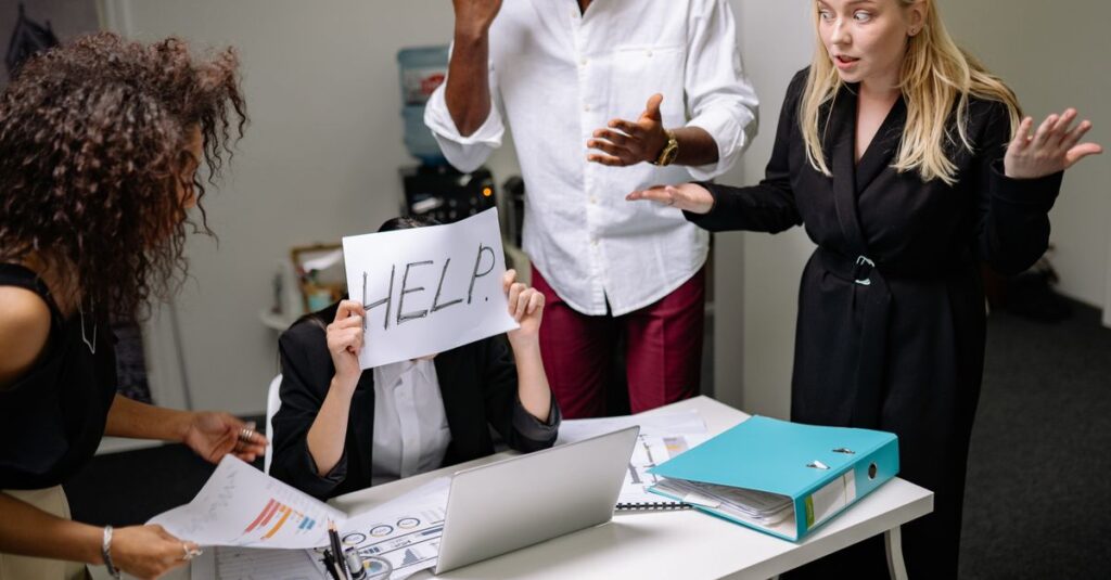 A group of employees in heated discussion, one holding a 'HELP' sign, indicates workplace stress.
