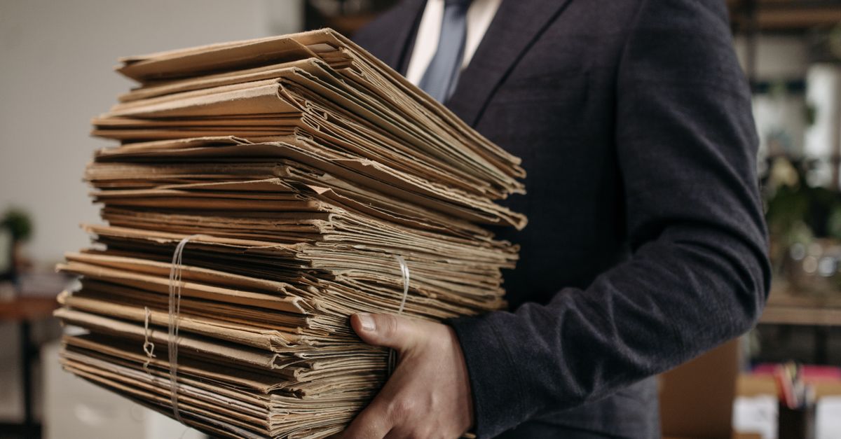 Close-up of business professional holding a large stack of brown folders in an office setting.