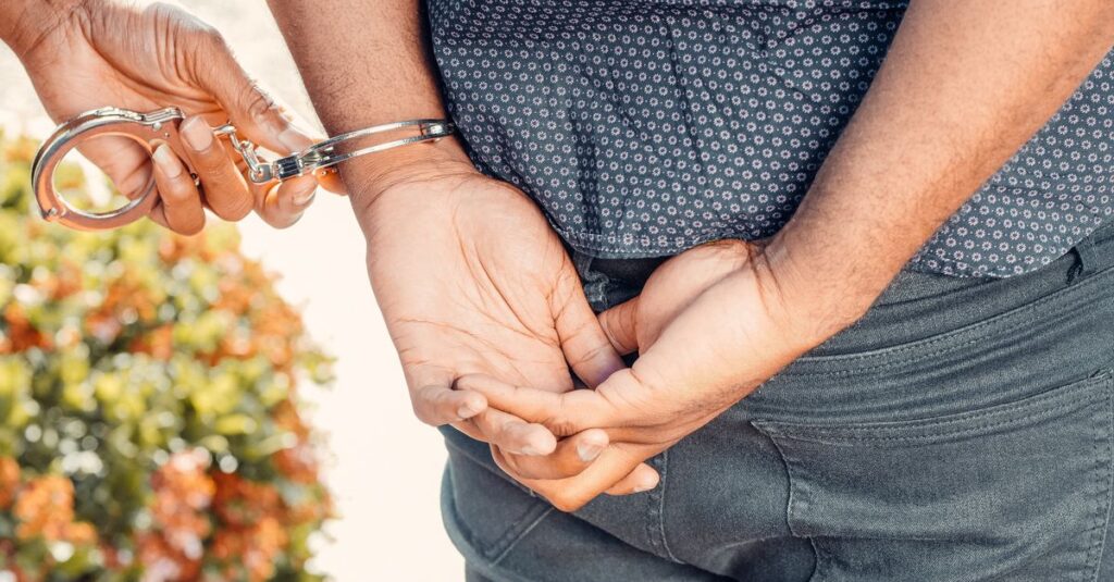 Close-up of hands in handcuffs during an arrest by police officer outdoors.