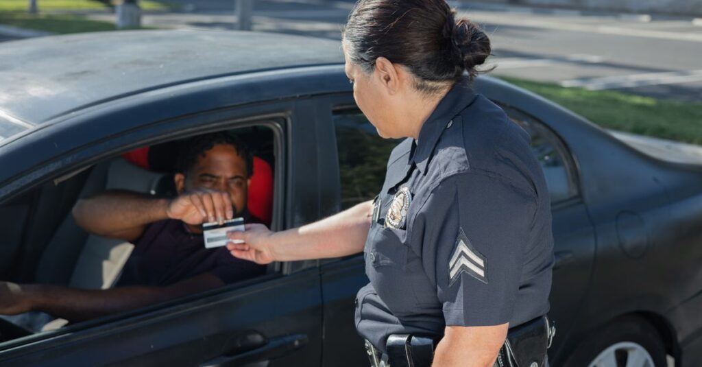 A police officer hands a ticket to a driver in a car on a sunny day street.