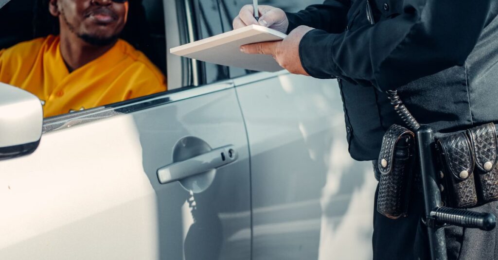 A police officer writes a ticket for a driver in a car during a roadside stop.