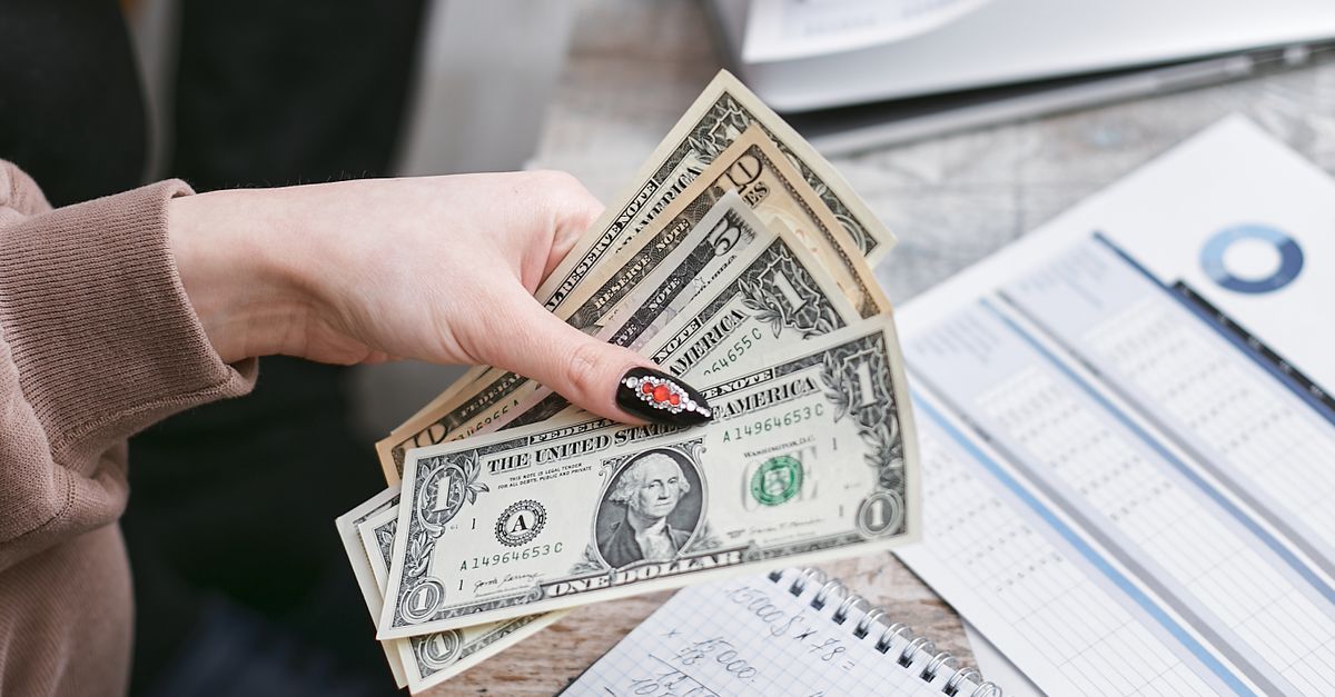 Two individuals counting dollar bills and reviewing financial documents indoors.